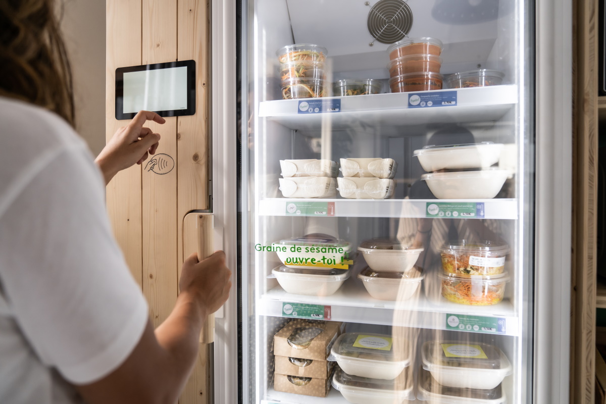 personne utilisant l'interface tactile d'une cantine connectée PopChef remplie de conteneurs alimentaires
