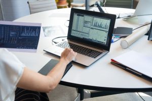 Business person evaluating financial charts on a laptop in a modern office setting.